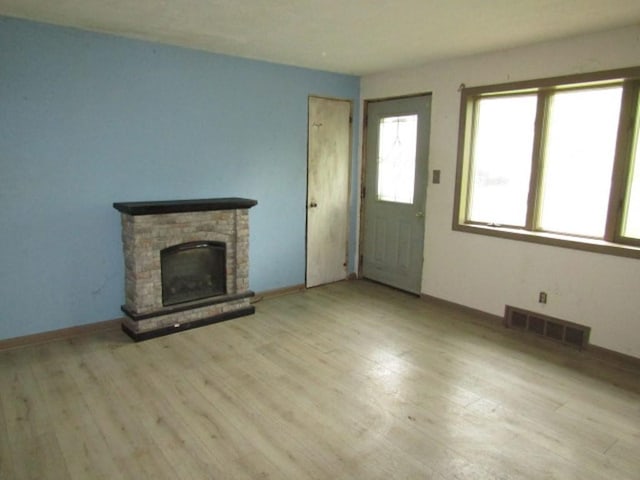 unfurnished living room with a stone fireplace and light hardwood / wood-style floors