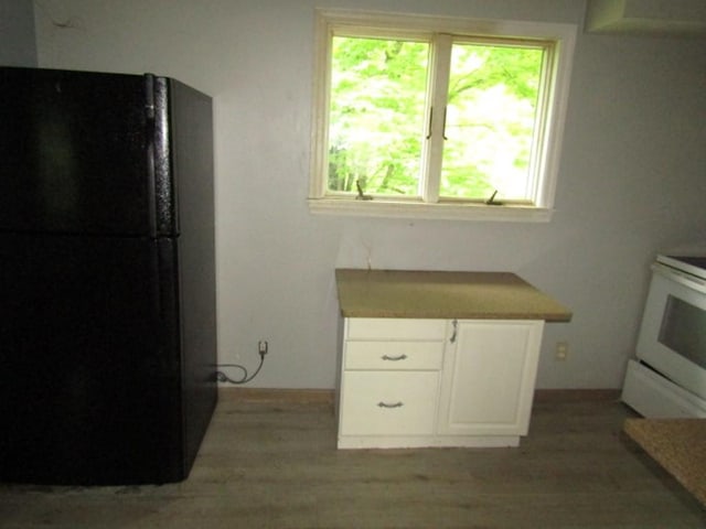 kitchen featuring white cabinetry, black fridge, white electric range, and light hardwood / wood-style floors