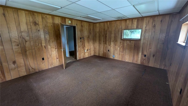 carpeted spare room featuring wood walls and a paneled ceiling