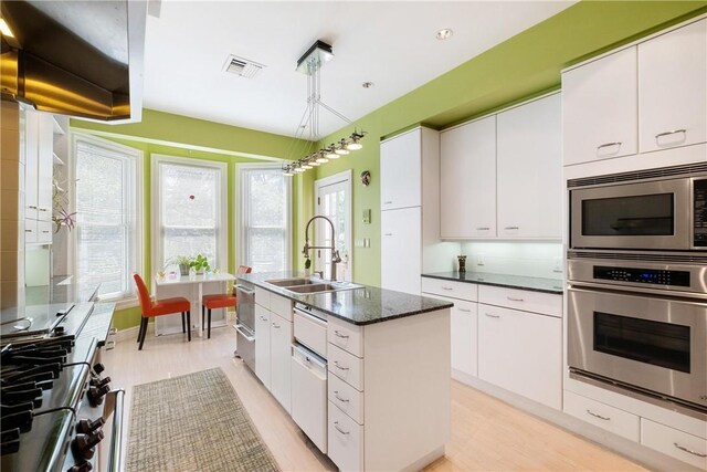 kitchen featuring stainless steel appliances, white cabinets, sink, a center island with sink, and light hardwood / wood-style flooring