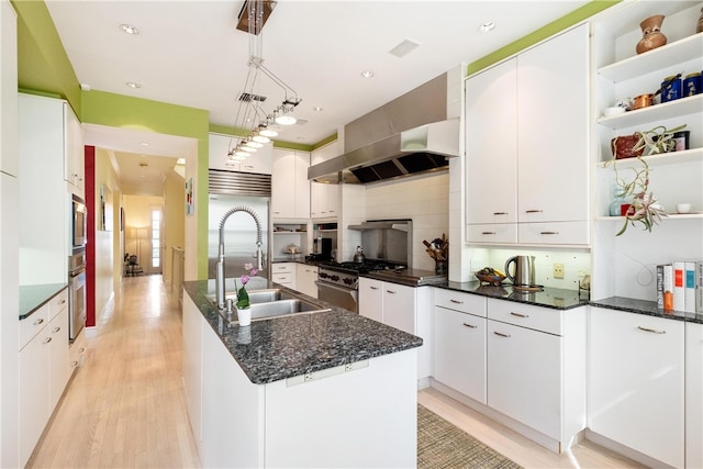 kitchen featuring white cabinets, a kitchen island with sink, appliances with stainless steel finishes, decorative backsplash, and decorative light fixtures