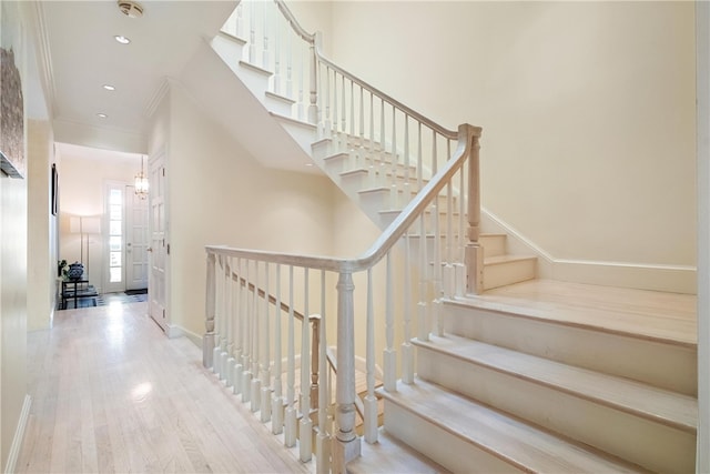 stairway with crown molding and light hardwood / wood-style flooring