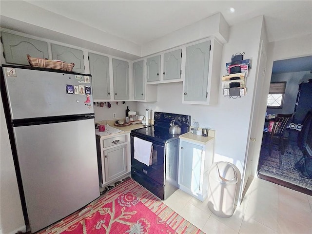 kitchen with black range with electric stovetop, stainless steel refrigerator, and white cabinets