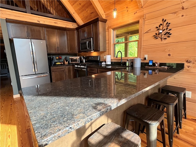 kitchen featuring vaulted ceiling with beams, light wood-type flooring, dark stone counters, hanging light fixtures, and appliances with stainless steel finishes