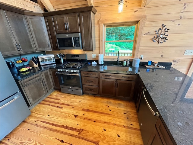 kitchen with dark stone countertops, light hardwood / wood-style floors, appliances with stainless steel finishes, dark brown cabinetry, and sink