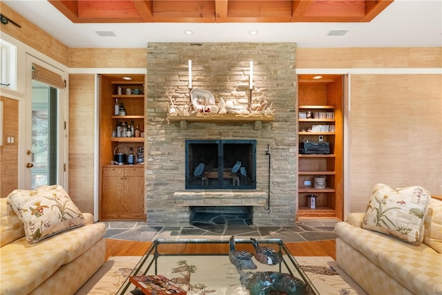 living room with beam ceiling, a stone fireplace, wood-type flooring, and built in shelves