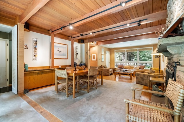 dining room with beam ceiling, a stone fireplace, rail lighting, and wood ceiling