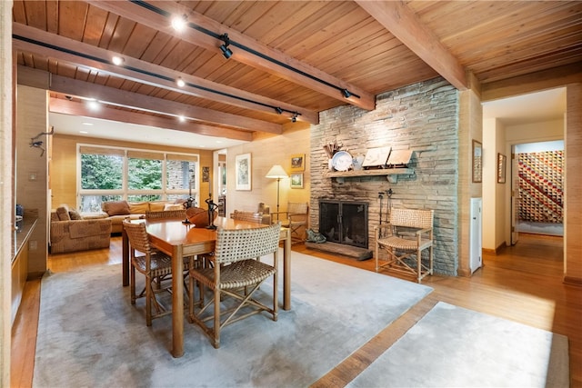 dining area with wood ceiling, beam ceiling, rail lighting, wood-type flooring, and a fireplace