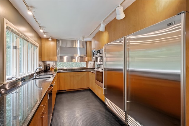 kitchen featuring stone counters, sink, appliances with stainless steel finishes, and wall chimney range hood