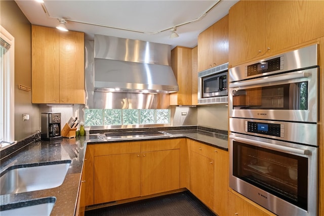 kitchen with rail lighting, wall chimney exhaust hood, appliances with stainless steel finishes, and dark stone counters