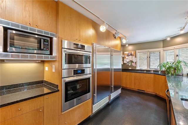 kitchen with track lighting, stainless steel appliances, and dark stone counters