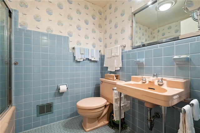 bathroom featuring tile walls, shower / bath combination with glass door, toilet, and tile patterned floors