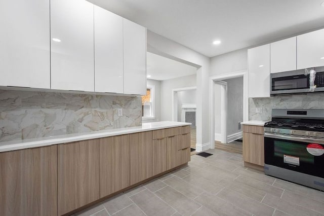 kitchen with white cabinets, backsplash, light hardwood / wood-style floors, and appliances with stainless steel finishes