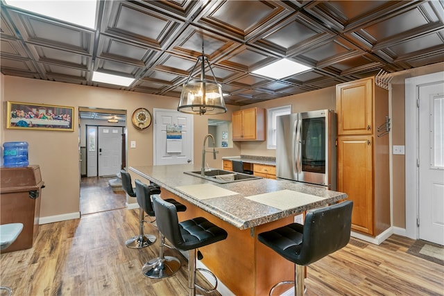 kitchen featuring light hardwood / wood-style flooring, hanging light fixtures, sink, stainless steel fridge, and a center island with sink