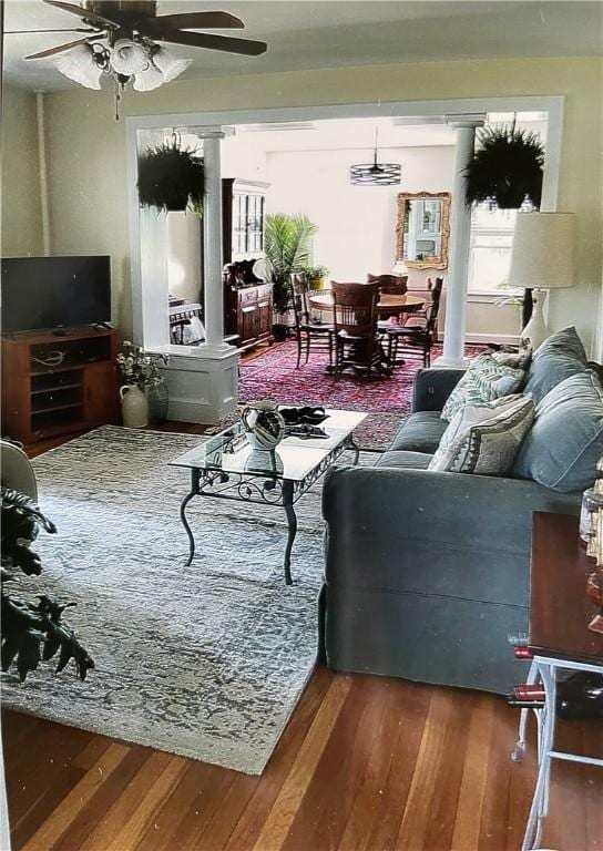 living area featuring a ceiling fan, decorative columns, and wood finished floors