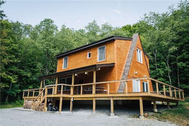 back of property featuring a deck, faux log siding, a shingled roof, and a view of trees