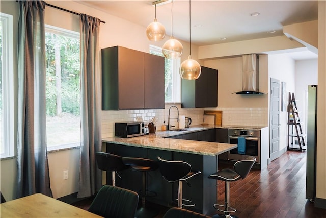 kitchen featuring backsplash, appliances with stainless steel finishes, a sink, light stone countertops, and wall chimney exhaust hood