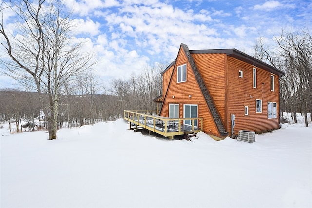 snow covered rear of property with faux log siding, a deck, and cooling unit