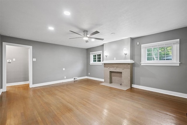 unfurnished living room with wood-type flooring, a stone fireplace, and ceiling fan