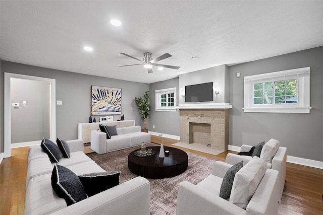 living room with a stone fireplace, wood-type flooring, and ceiling fan