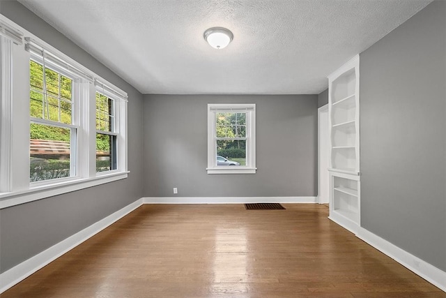 spare room with a textured ceiling, built in shelves, and wood-type flooring