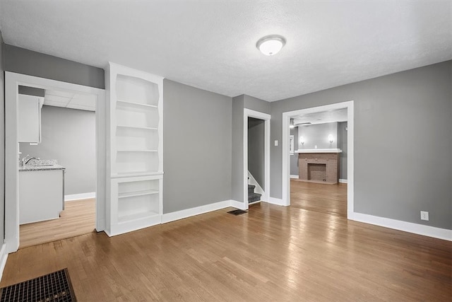 unfurnished living room featuring built in features, hardwood / wood-style floors, sink, a textured ceiling, and a brick fireplace