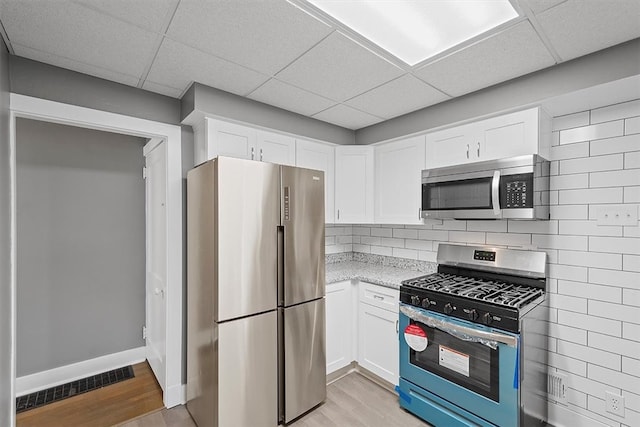 kitchen featuring a drop ceiling, light stone counters, light wood-type flooring, and stainless steel appliances