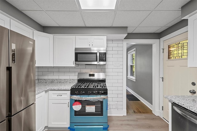 kitchen with appliances with stainless steel finishes, a paneled ceiling, white cabinets, decorative backsplash, and light wood-type flooring