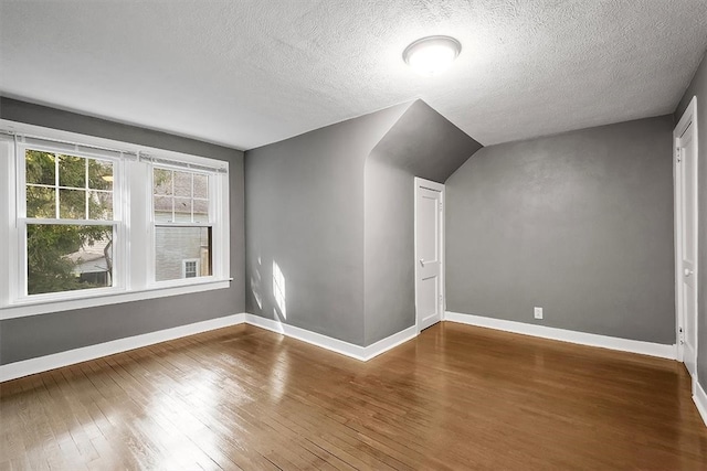 spare room featuring lofted ceiling, a textured ceiling, and wood-type flooring