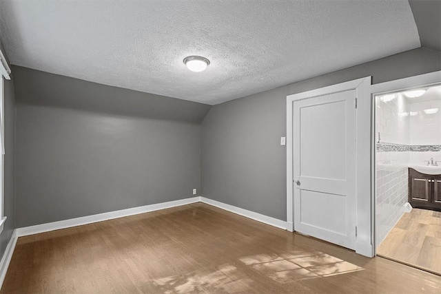 unfurnished bedroom featuring hardwood / wood-style flooring, vaulted ceiling, sink, and a textured ceiling