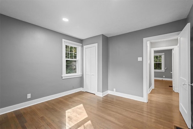 unfurnished bedroom with a closet, multiple windows, and light wood-type flooring