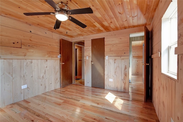 unfurnished room with wooden walls, light wood-type flooring, and ceiling fan