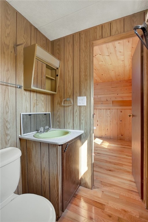 bathroom with vanity, wooden walls, wood-type flooring, and toilet