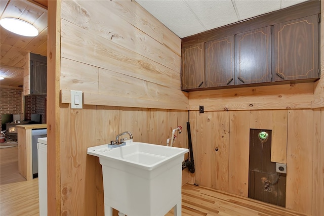 laundry area with sink, wood walls, and light wood-type flooring