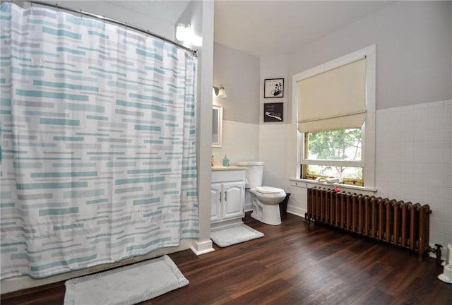 bathroom with toilet, tile walls, vanity, radiator, and hardwood / wood-style flooring