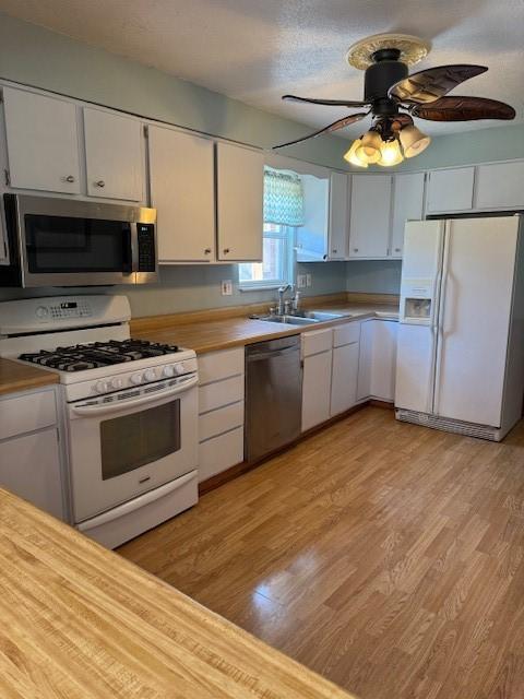 kitchen featuring light wood finished floors, white cabinetry, a sink, and appliances with stainless steel finishes