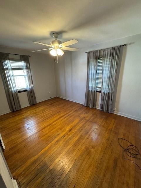 empty room featuring hardwood / wood-style floors, baseboards, and a ceiling fan