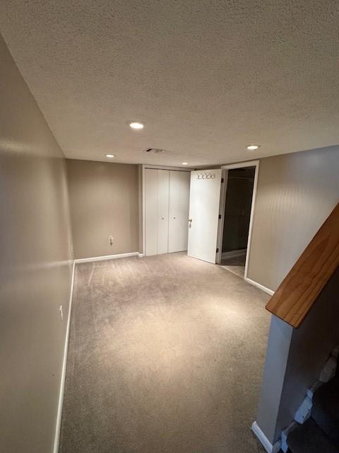 basement featuring a textured ceiling, baseboards, carpet, and recessed lighting