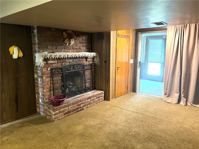 unfurnished living room with wooden walls, carpet, and a brick fireplace