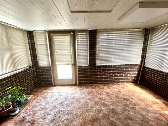 unfurnished room featuring carpet flooring, wooden ceiling, and brick wall