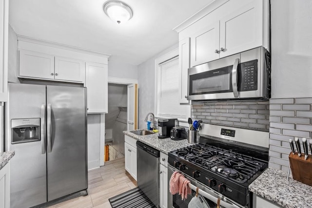 kitchen featuring white cabinetry, sink, light stone countertops, appliances with stainless steel finishes, and backsplash