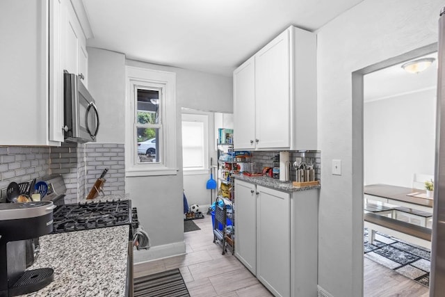 kitchen with appliances with stainless steel finishes, light hardwood / wood-style flooring, white cabinets, light stone counters, and backsplash