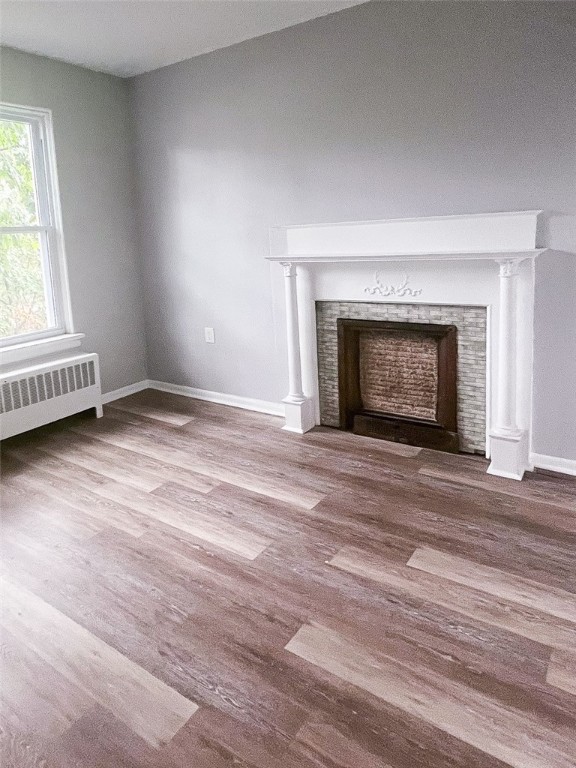 unfurnished living room featuring ornate columns, radiator, and hardwood / wood-style floors