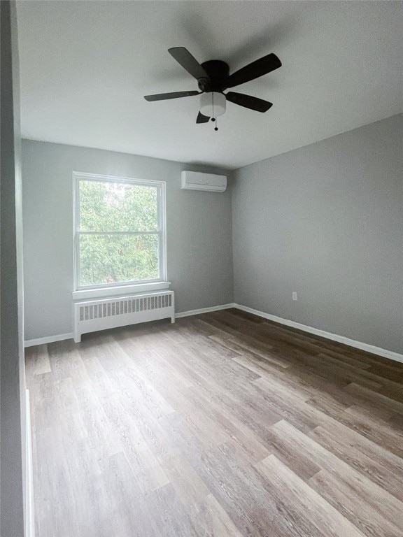 spare room with a wall mounted AC, radiator heating unit, hardwood / wood-style flooring, and ceiling fan