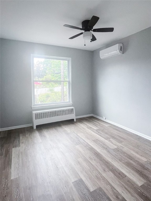 spare room with radiator heating unit, a wall mounted air conditioner, ceiling fan, and hardwood / wood-style floors