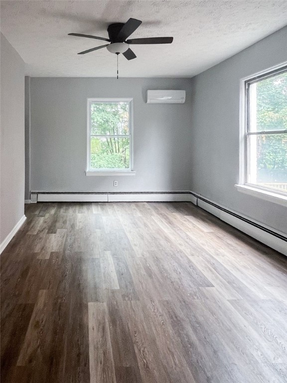 empty room with a wall mounted air conditioner, wood-type flooring, ceiling fan, and a healthy amount of sunlight