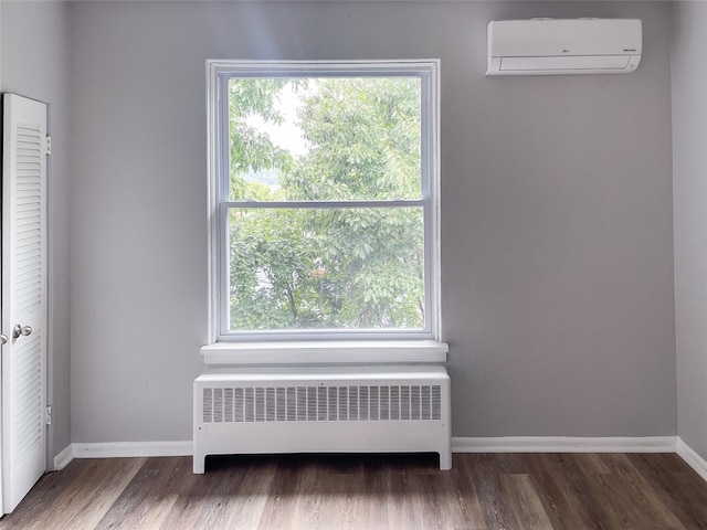 unfurnished room featuring radiator heating unit, a wall mounted air conditioner, a wealth of natural light, and wood-type flooring