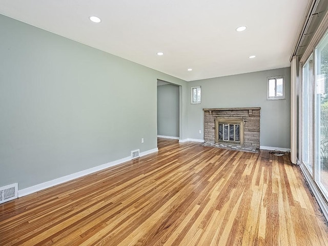 unfurnished living room with a stone fireplace and light hardwood / wood-style floors