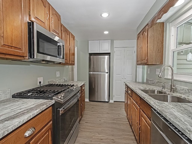 kitchen featuring stainless steel appliances, sink, light stone counters, and light hardwood / wood-style floors