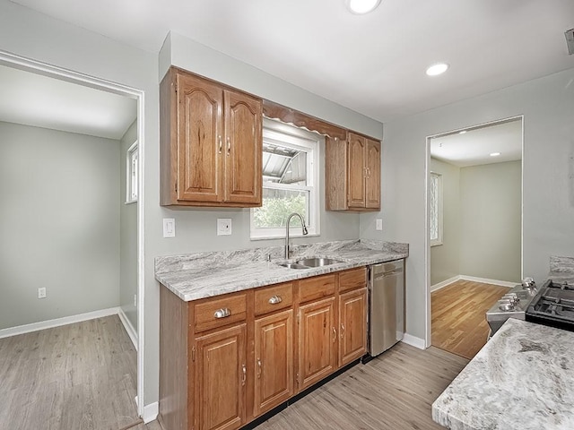 kitchen with stainless steel appliances, sink, light stone counters, and light wood-type flooring